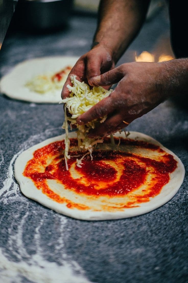 Molho de tomate sendo espalhado sobre o disco de massa